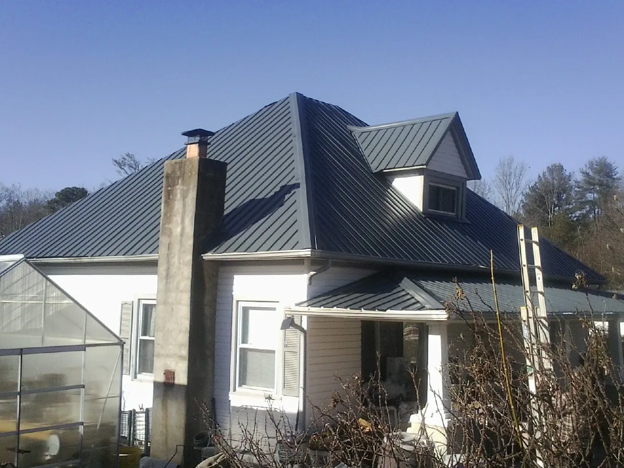 Dark blue standing seam metal roof on a white farmhouse with dormer — Slate & Tile Roof Repair by Roofing Brothers in Bretz
