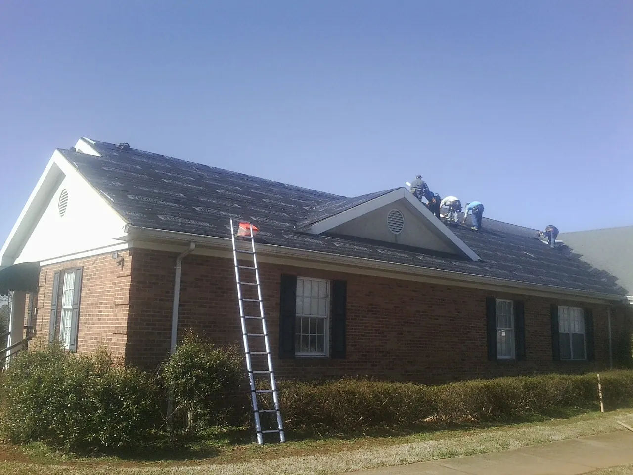 Crew tearing shingles off a brick ranch roof with a ladder set — Emergency Roof Repair work by our crew in Bretz
