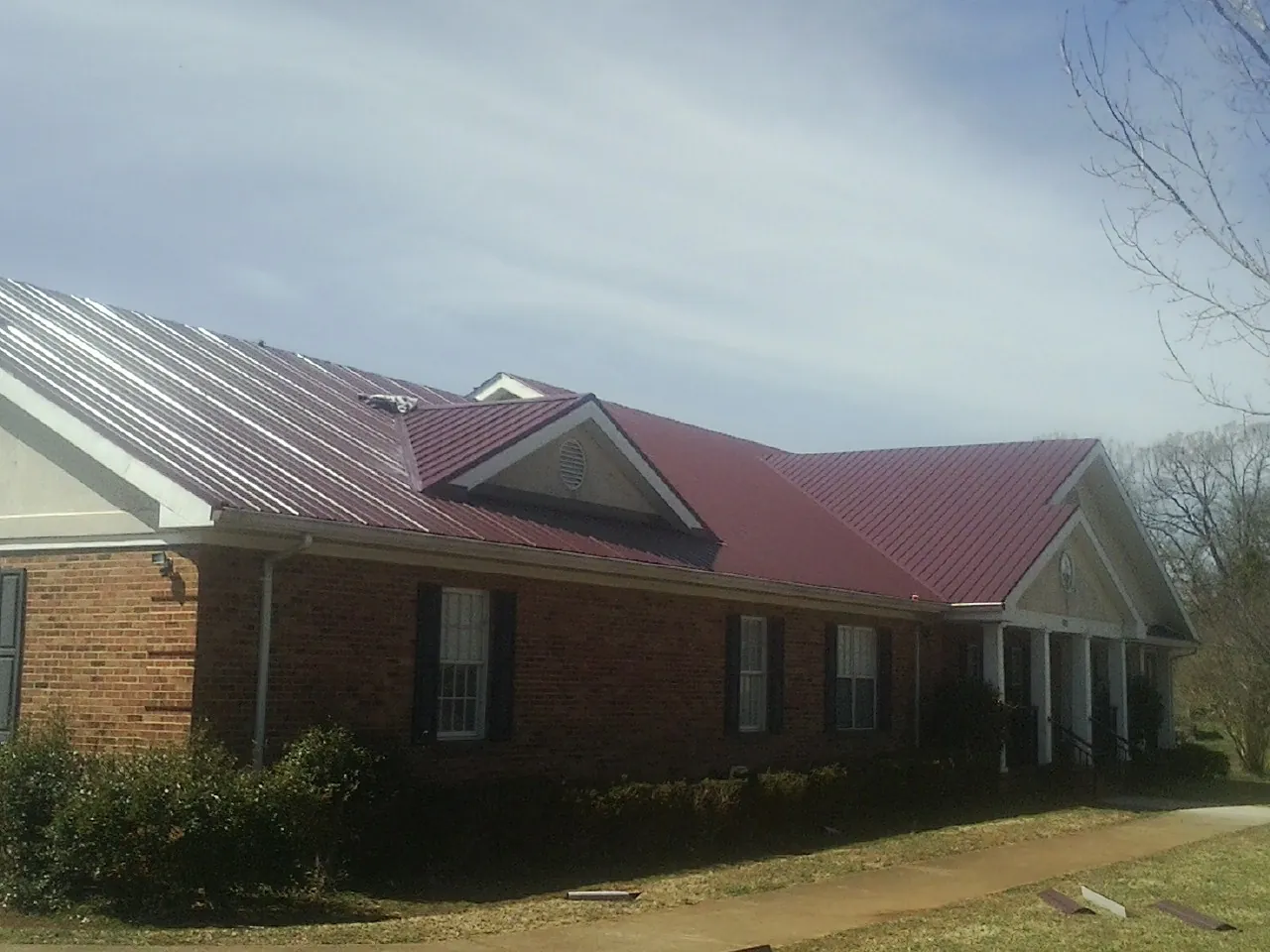 Red metal roof with gabled entries on a long brick building, from a Hail Damage Roof Repair job in Bretz