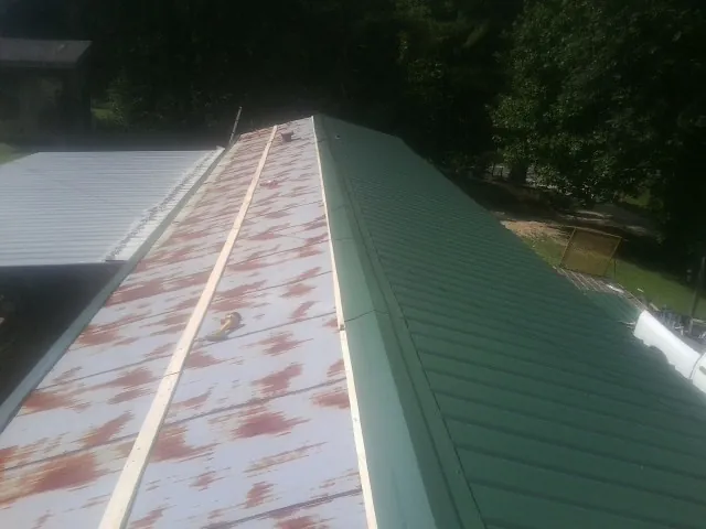 Old rusted panels beside newly installed green metal roofing — Wind Damage Roof Repair by Roofing Brothers in Bretz