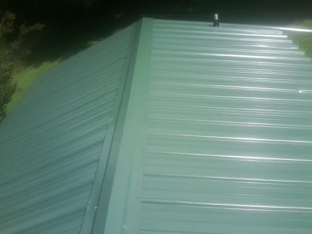 New green metal panels meeting at the ridge of a roof — Flat Roof Repair work by our crew in Bretz