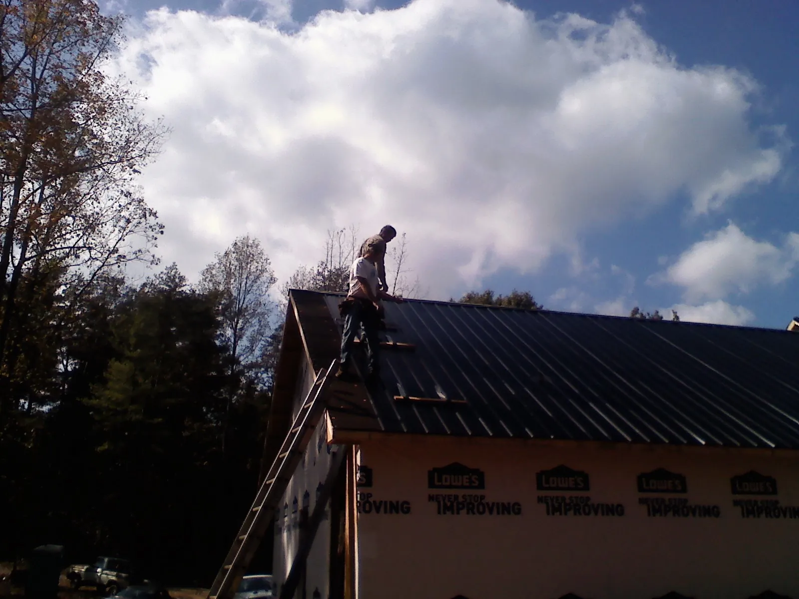 Roofer fastening dark metal panels high against a cloudy sky, from a Roof Inspection job in Bretz