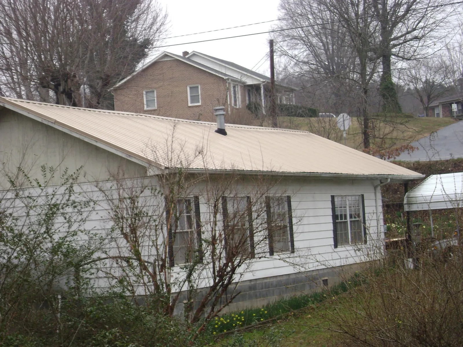 Tan metal roof on a white sided house set into a hillside — Commercial Roofing by Roofing Brothers in Bretz