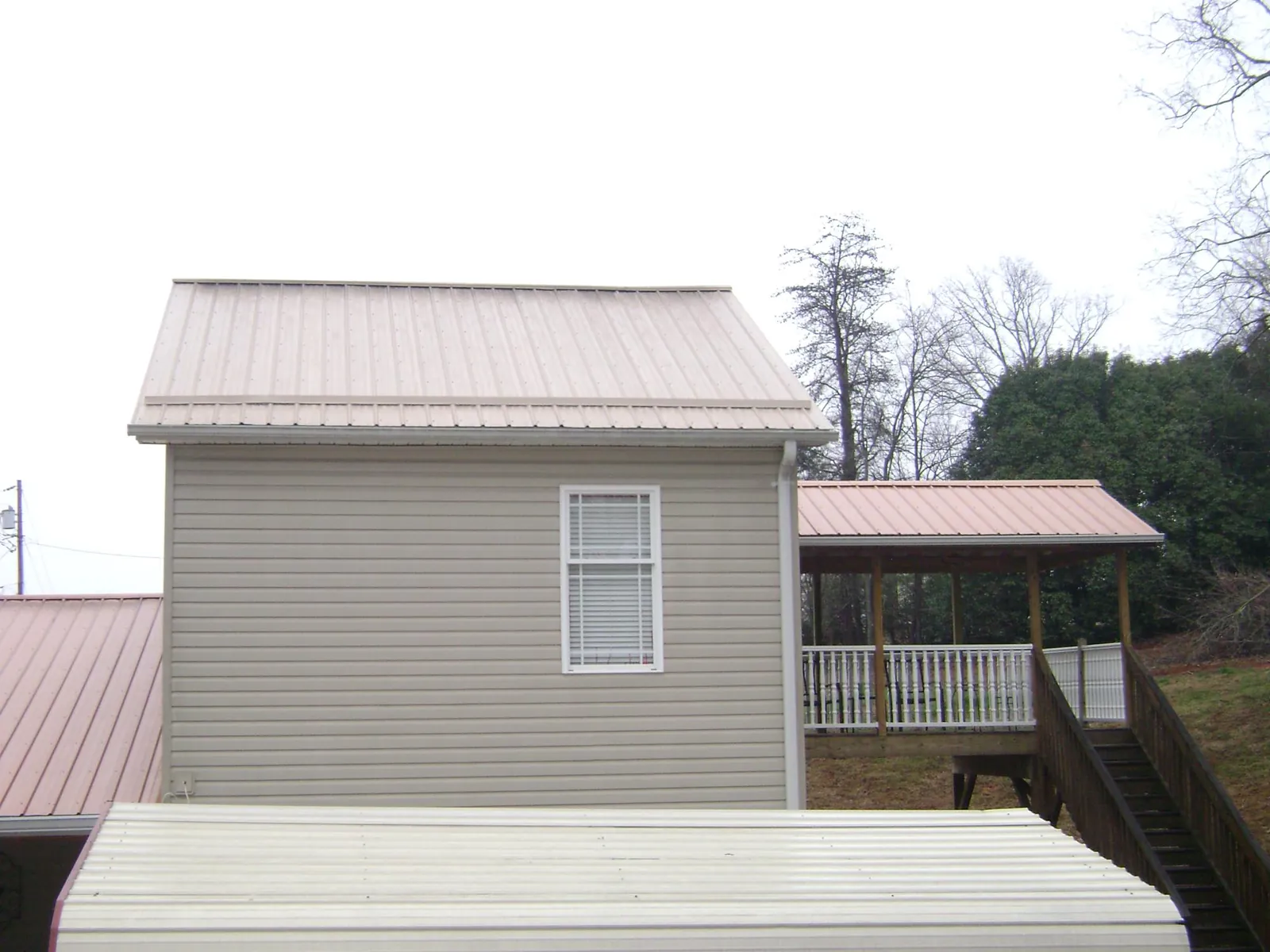 Tan metal roofs on a two story addition and attached porch, from a Roof Replacement job in Bretz